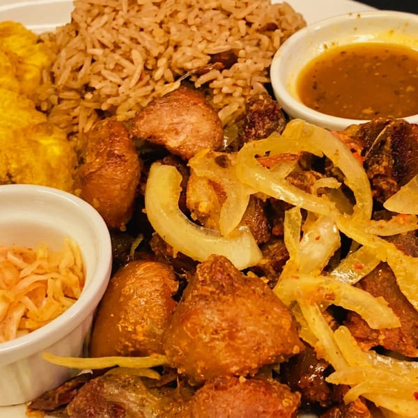 Fried pork with onions, rice, plantains, and two small bowls of sauce and pickled vegetables.