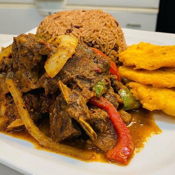 Curried goat with rice and peas, and fried plantains on a white rectangular plate.