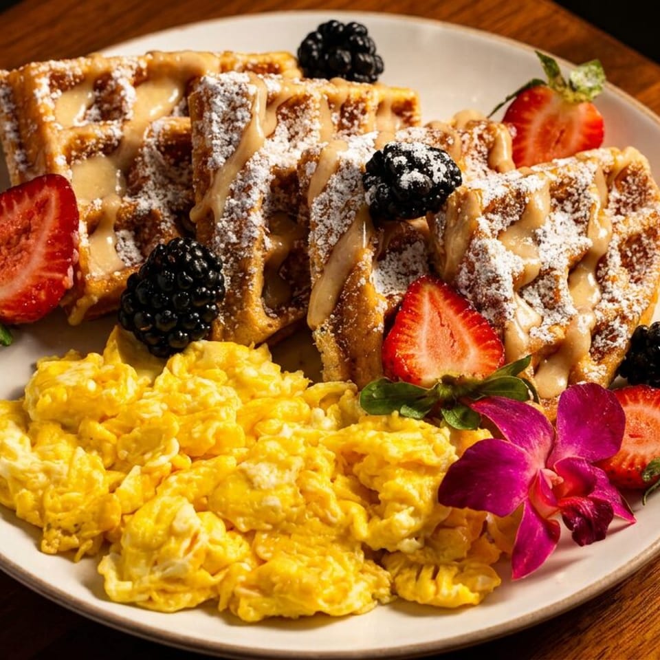 A breakfast plate with waffles, scrambled eggs, strawberries, blackberries, and an orchid garnish.